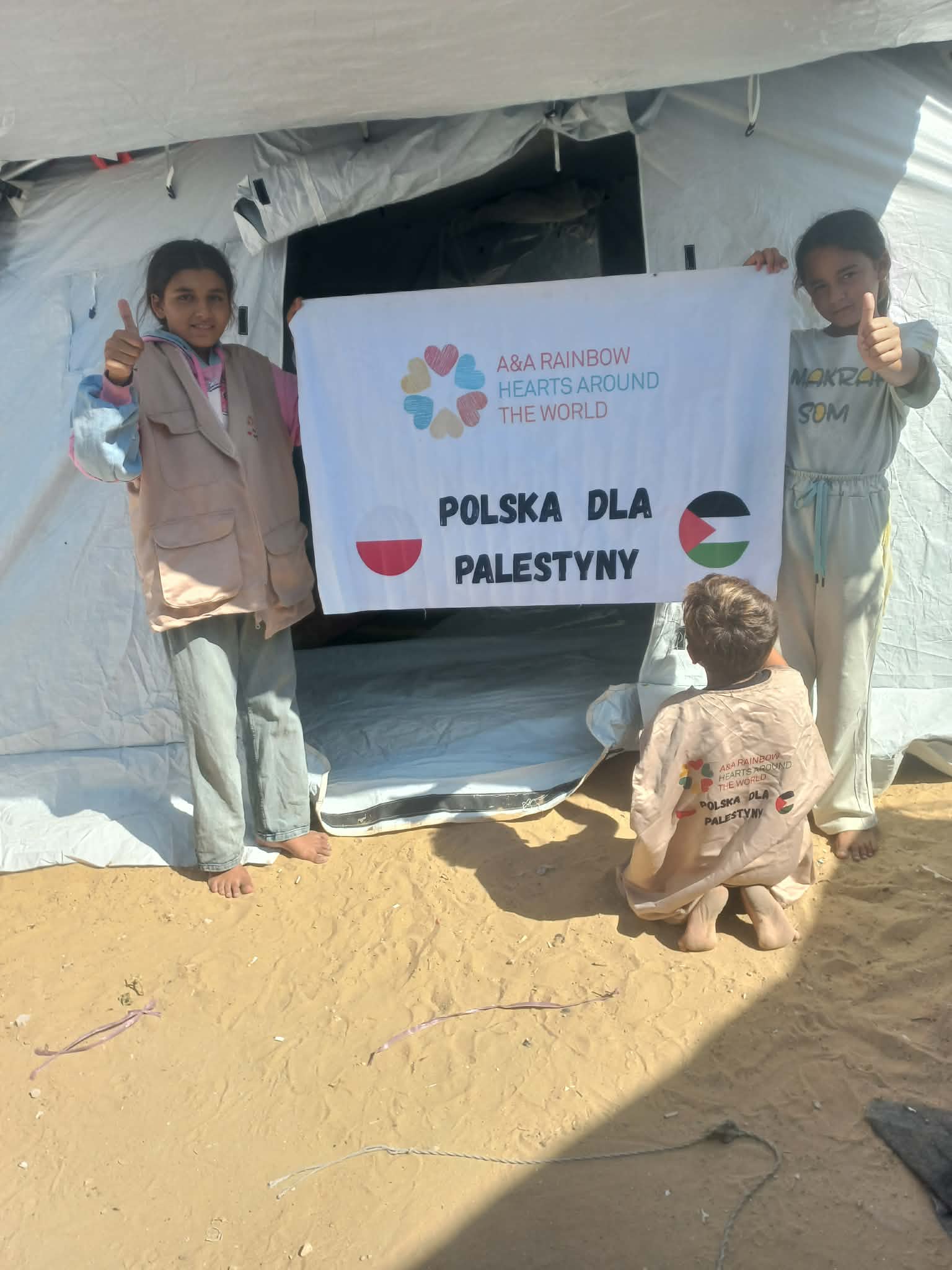 617 ton pomocy wjechało do Gazy. Noursan z siostrą trzymają transparent z napisem "Polska dla Palestyny" a ich braciszek siedzi przed nimi w kamizelce naszego wolontariusza.